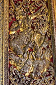 Wat Xieng Thong temple in Luang Prabang, Laos. Detail of a wooden door of the sim with gilded carvings on a red background. 